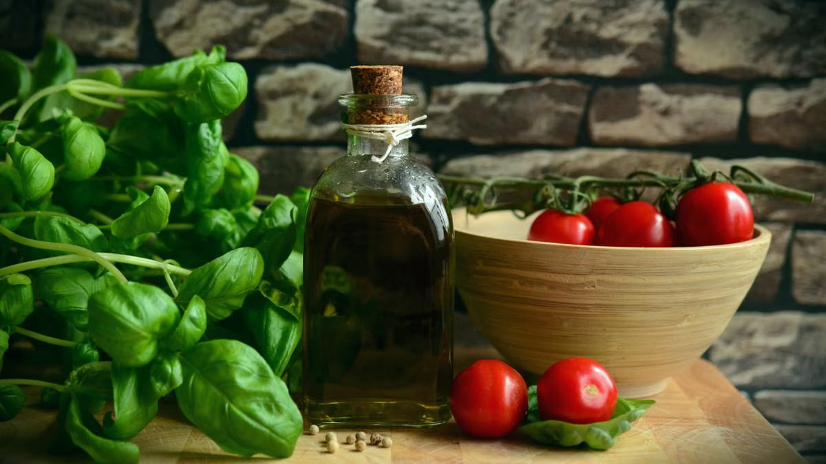 A rustic arrangement of fresh basil, ripe tomatoes, and olive oil on a wooden surface.